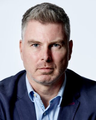 Professional headshot of a man with grey hair wearing a navy blazer.