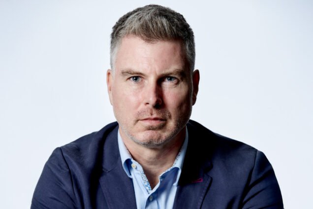 Professional headshot of a man with grey hair wearing a navy blazer.