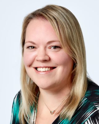 Professional headshot of a smiling blonde woman, wearing a green and black top.