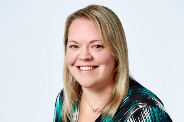 Professional headshot of a smiling blonde woman, wearing a green and black top.