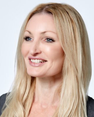 Professional headshot of a smiling blonde woman with blue eyes.