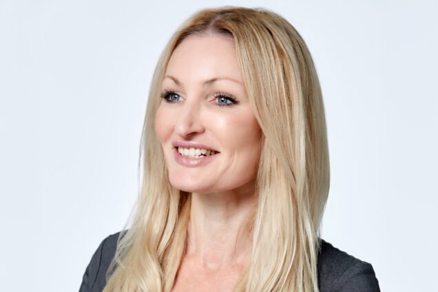 Professional headshot of a smiling blonde woman with blue eyes.