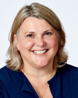 Headshot of a smiling woman with blonde hair, wearing a navy top.