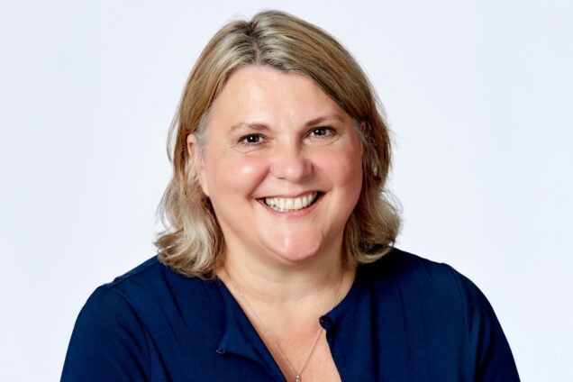 Headshot of a smiling woman with blonde hair, wearing a navy top.