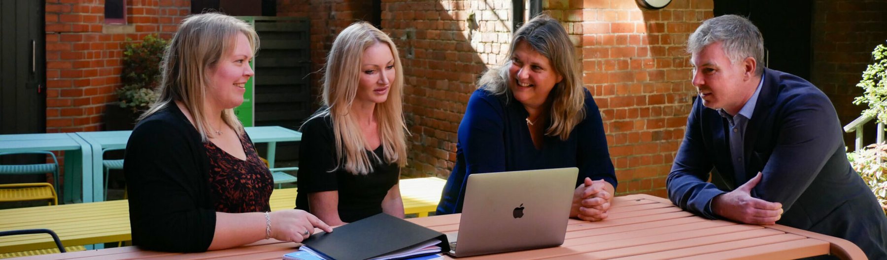 A team of four solicitors collaborating around a laptop at an outdoor table.